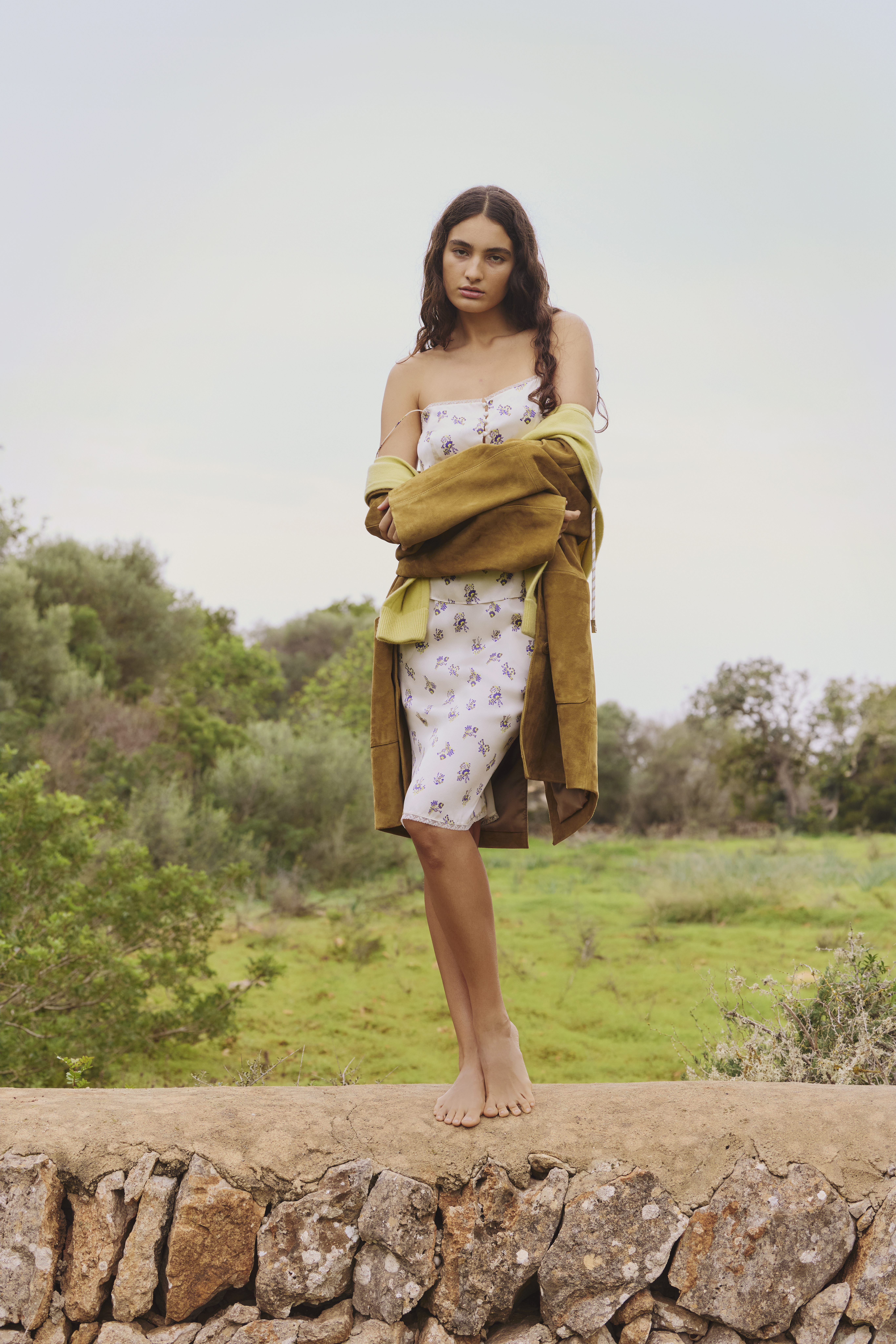 Woman standing on a stone wall wearing a Dorothee Schumacher Silk Set and suede coat