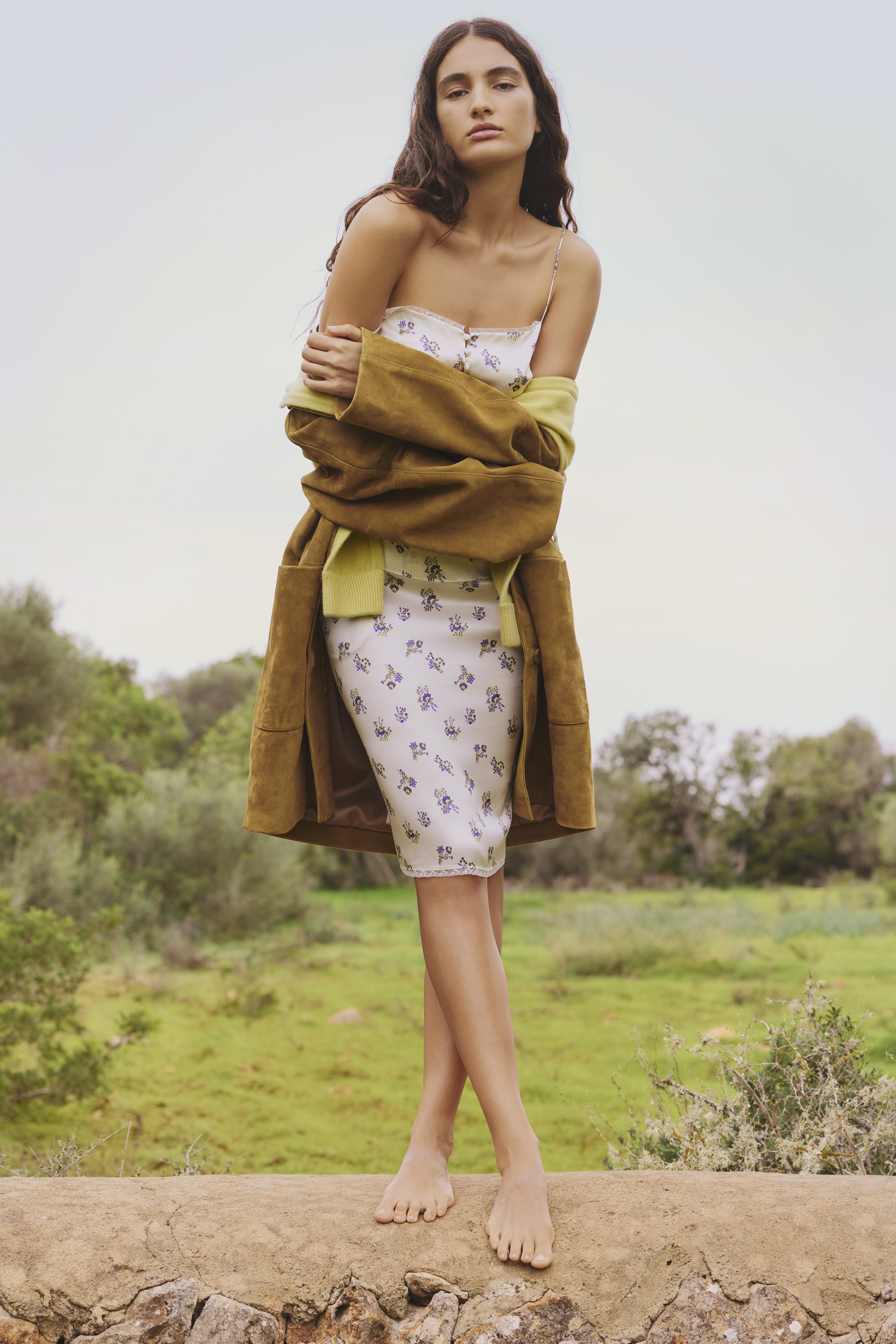 Woman standing on a stone wall wearing a suede coat and silk set from DOROTHEE SCHUMACHER