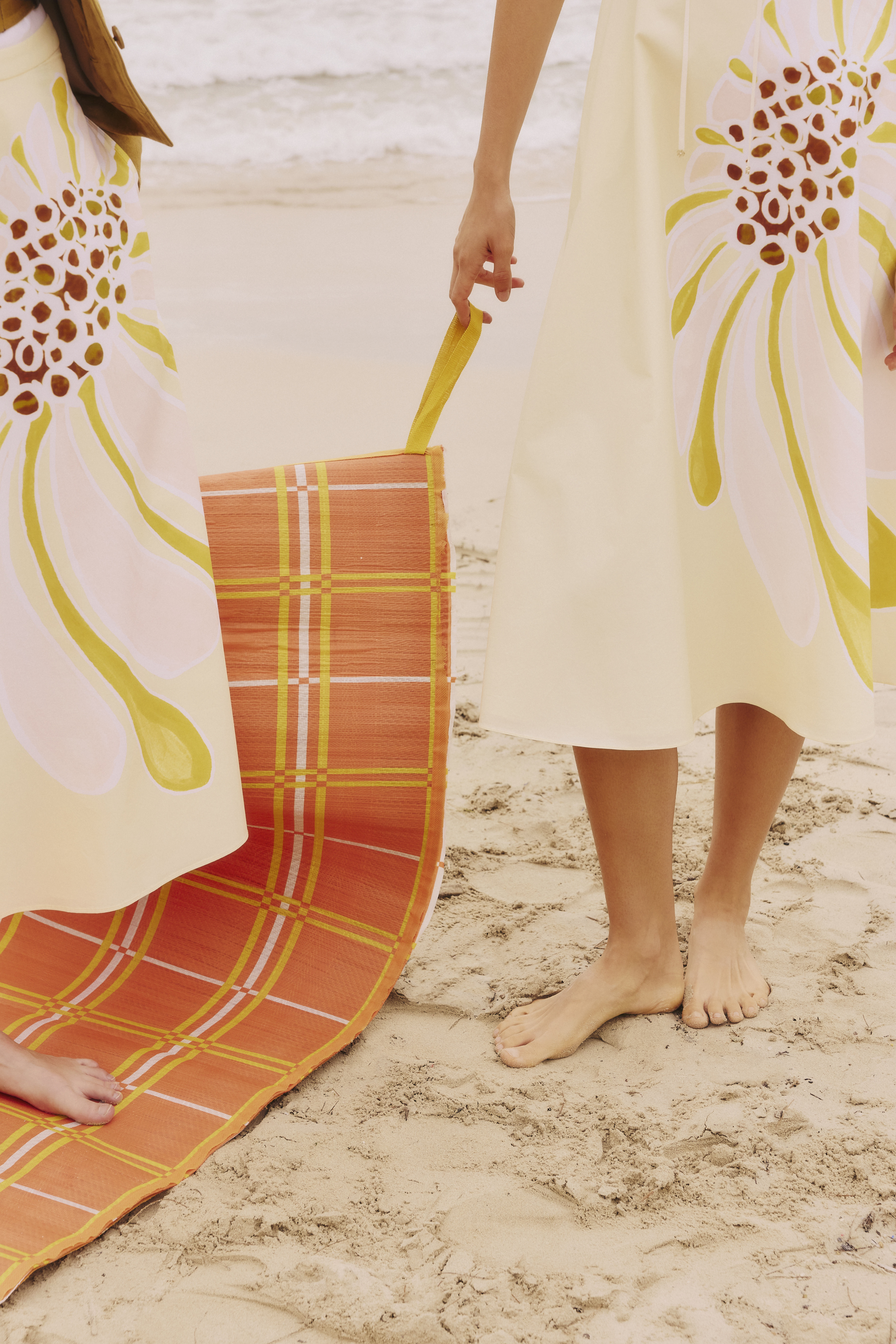 Crop of two women on the beach wearing a yellow floral print skirt 