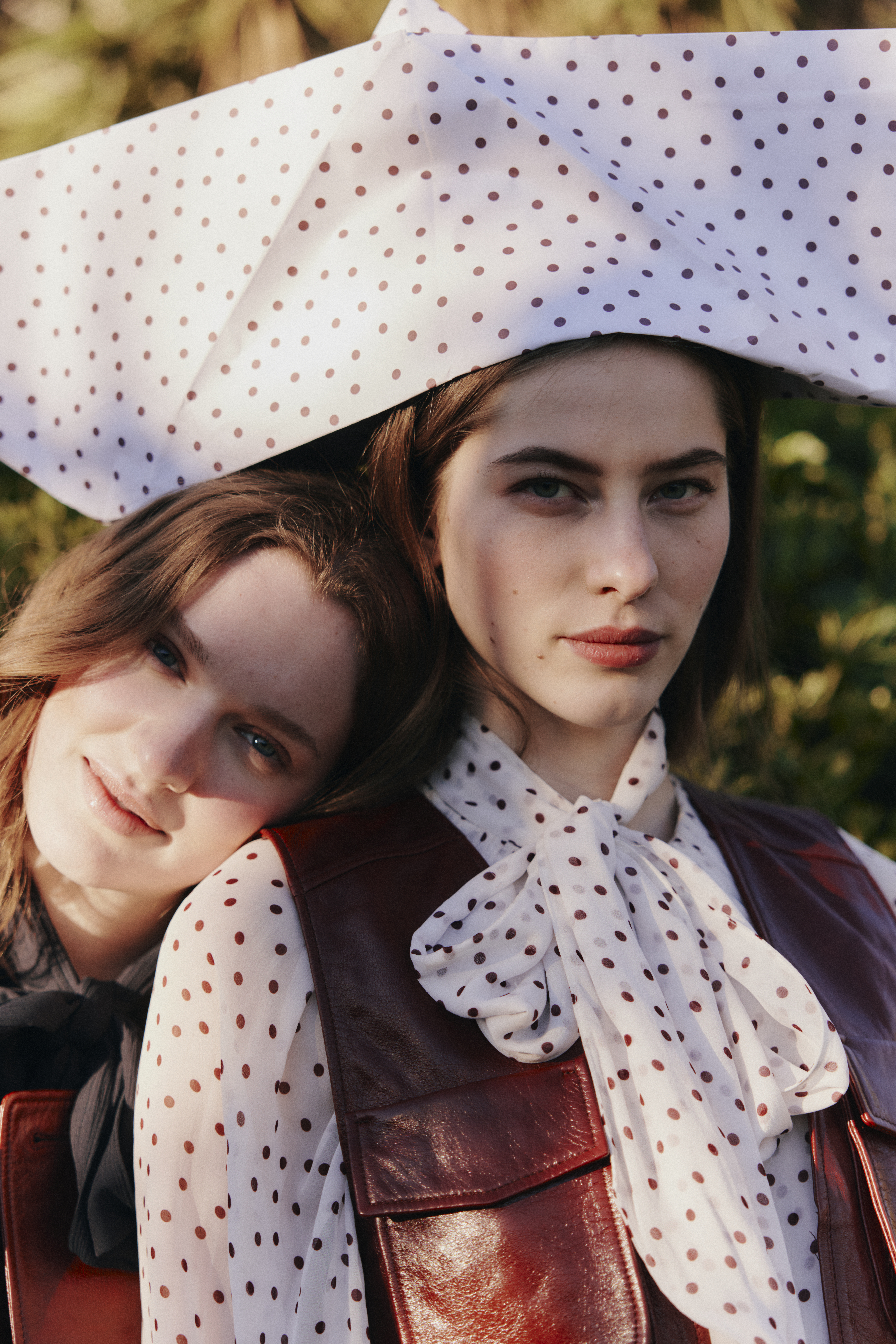 Two Models posing together wearing leather pieces and a blouse with a polka dot print. One of the models is balancing a giant paper boat in the same polka dot print on her head.