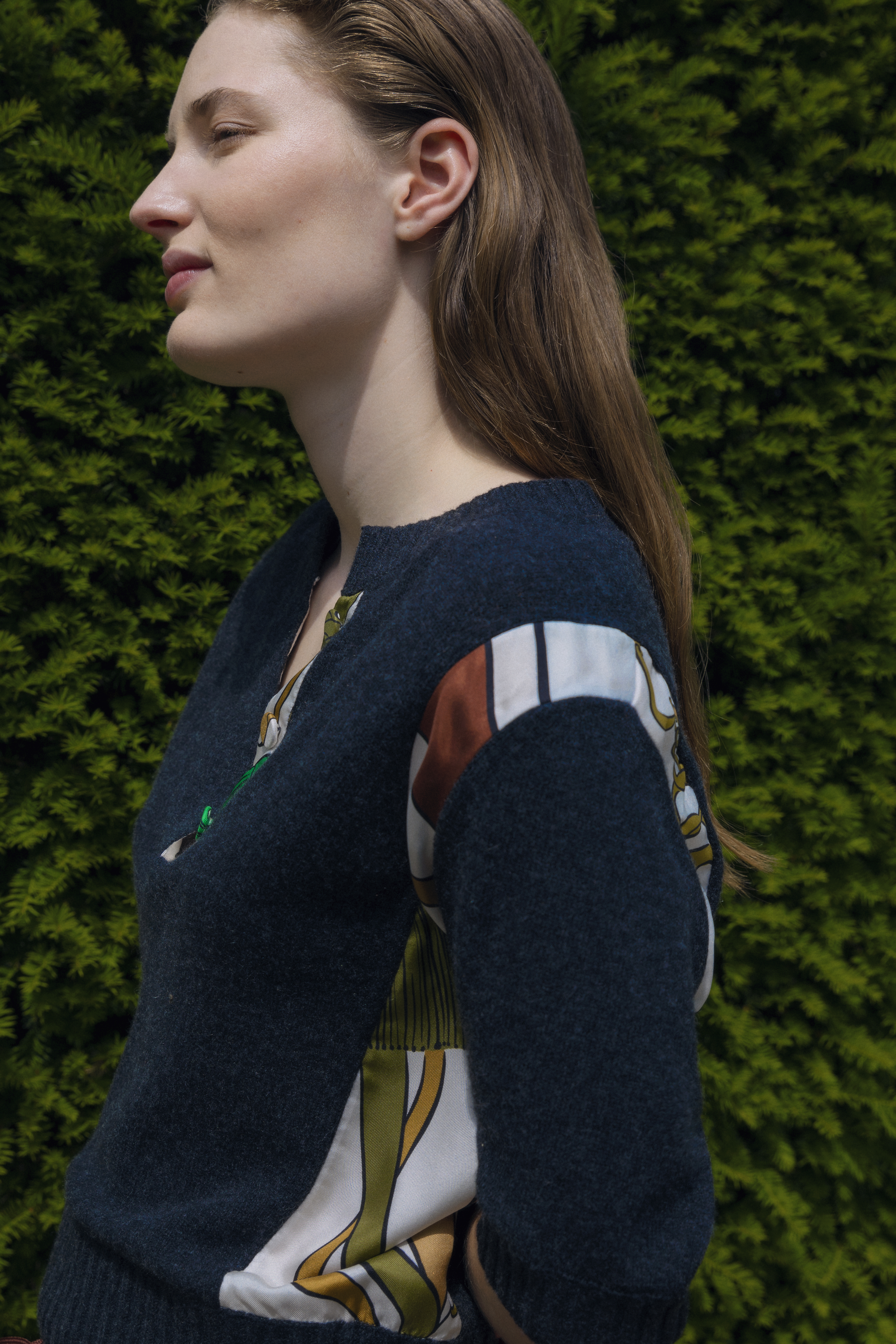 Model in DOROTHEE SCHUMACHER portrayed from the side while wearing a grey knit piece with satin patchwork sleeves