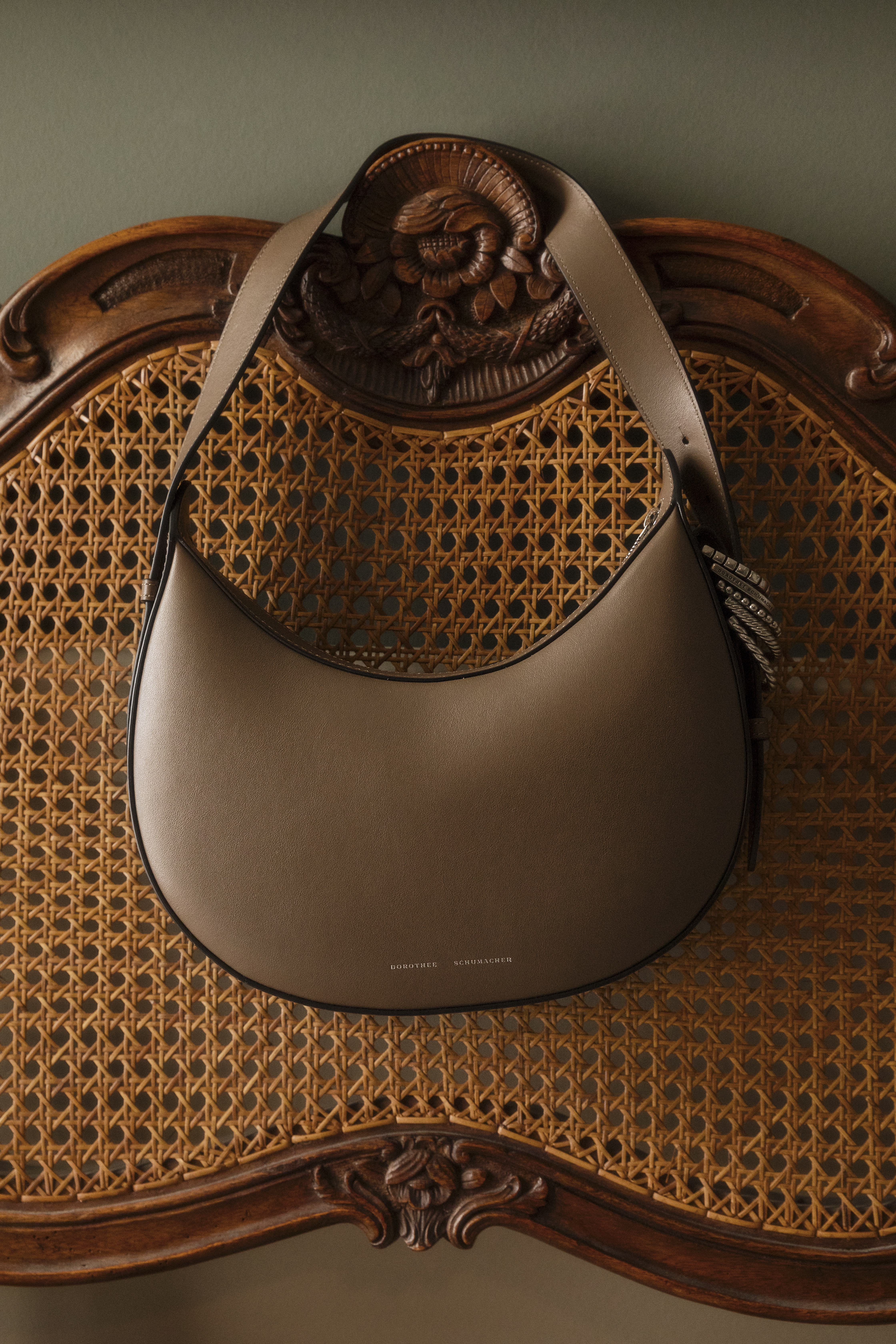 A taupe colored Half Moon Bag from Dorothe Schumacher hanging on a rattan chair