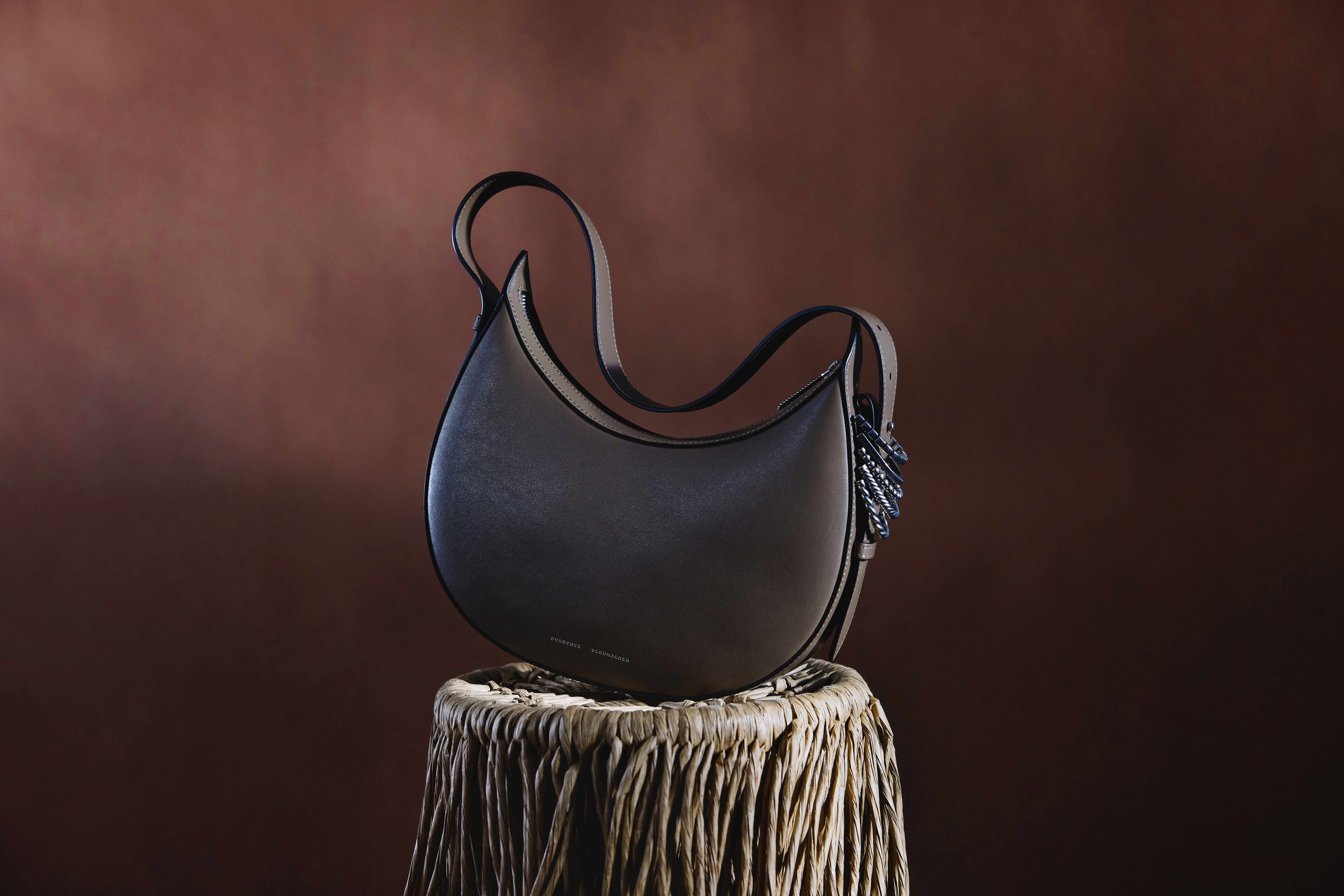 taupe leather half moon bag with silver details on the side on a strawy table