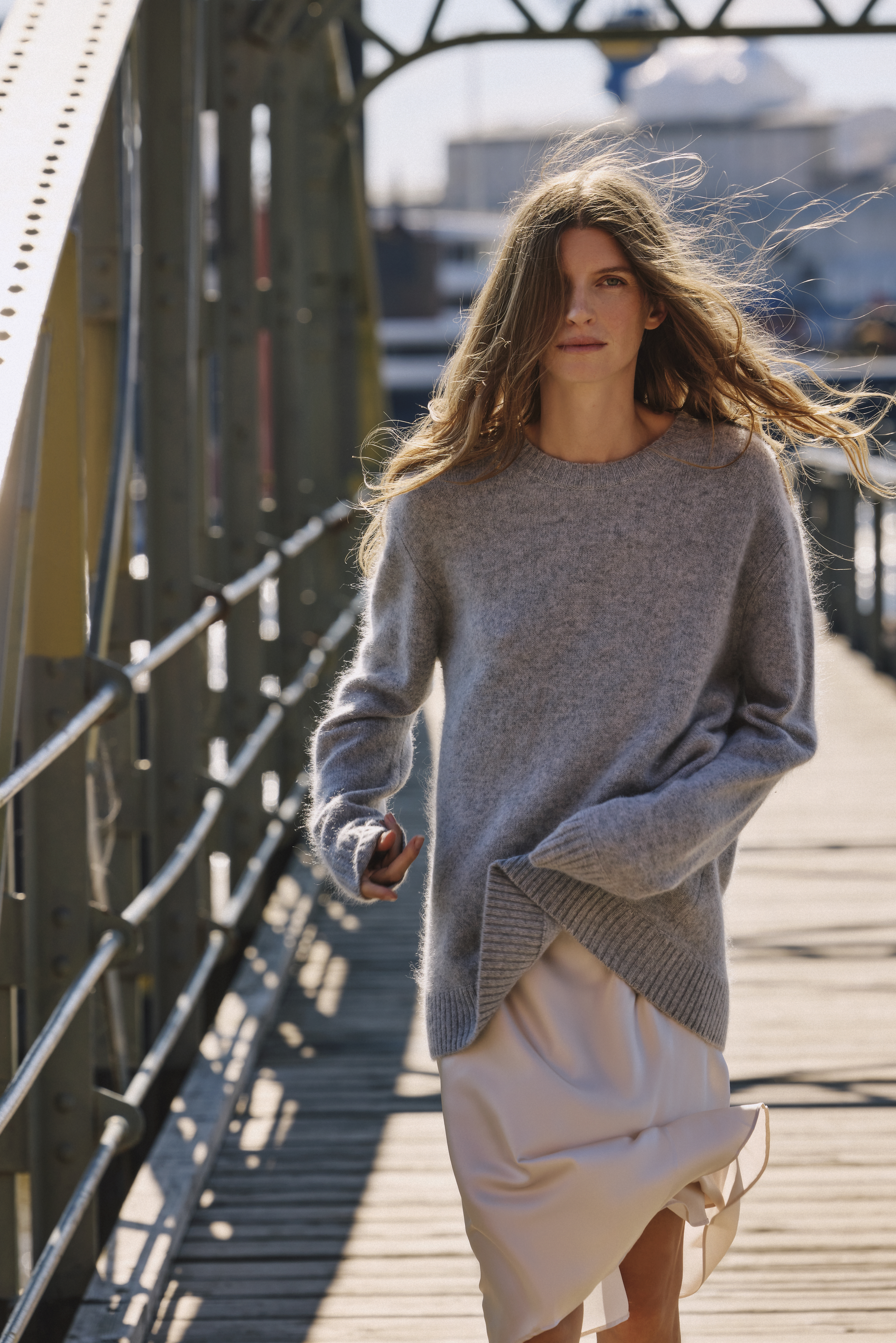 the woman is wearing a grey pullover and a white skirt in the wind