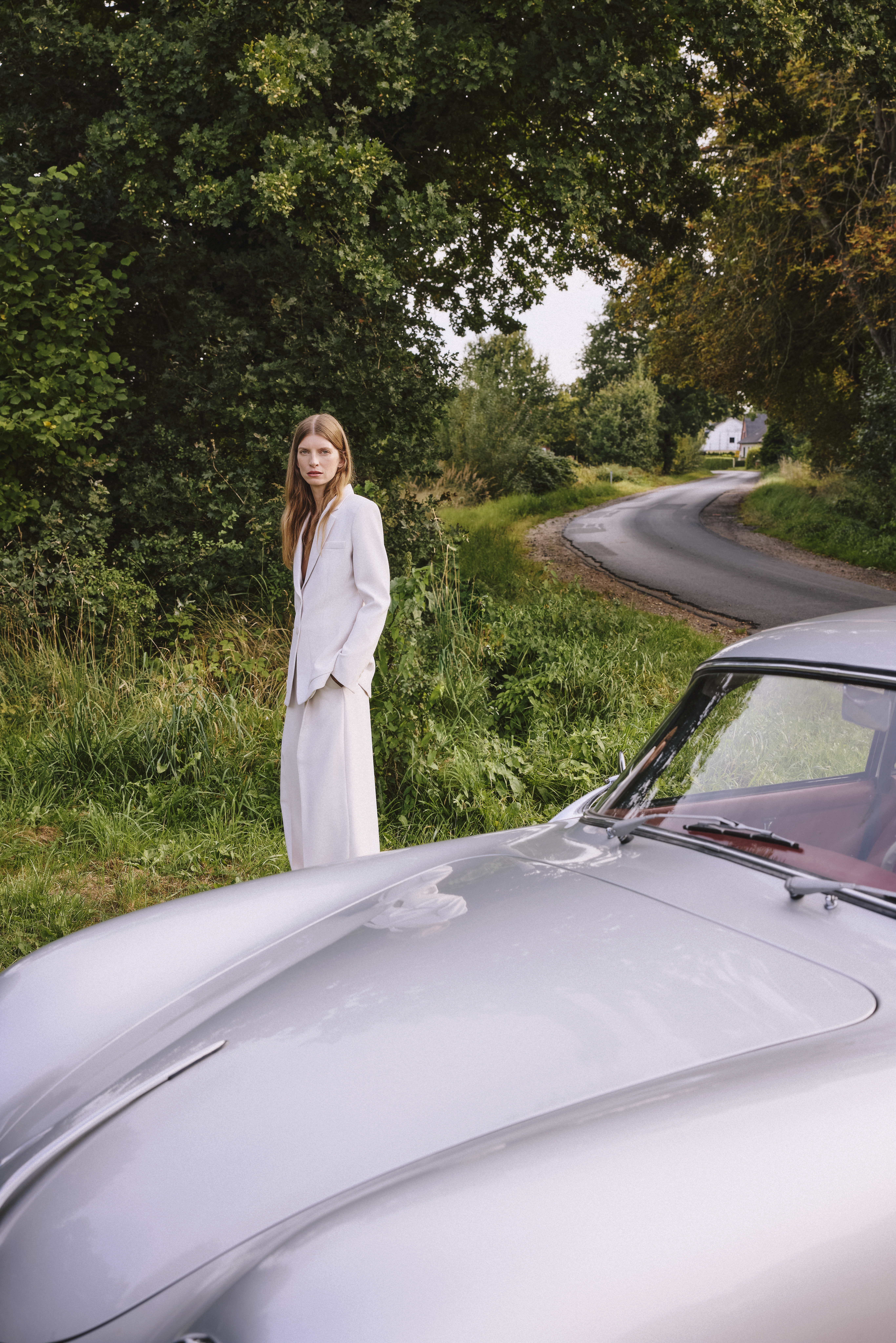 a woman is standing behind a car wearing a white suit