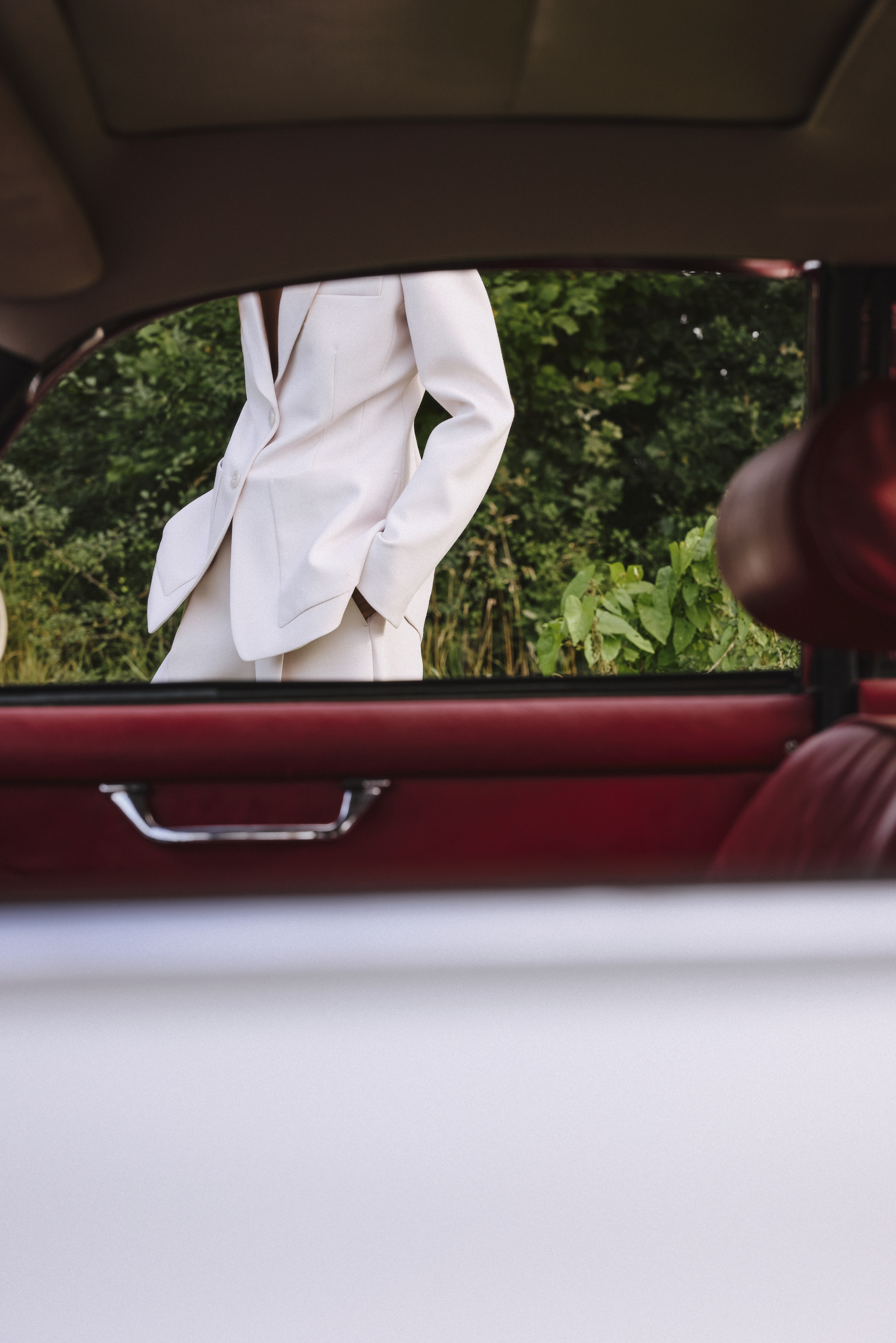 a woman is standing behind a car wearing a white suit