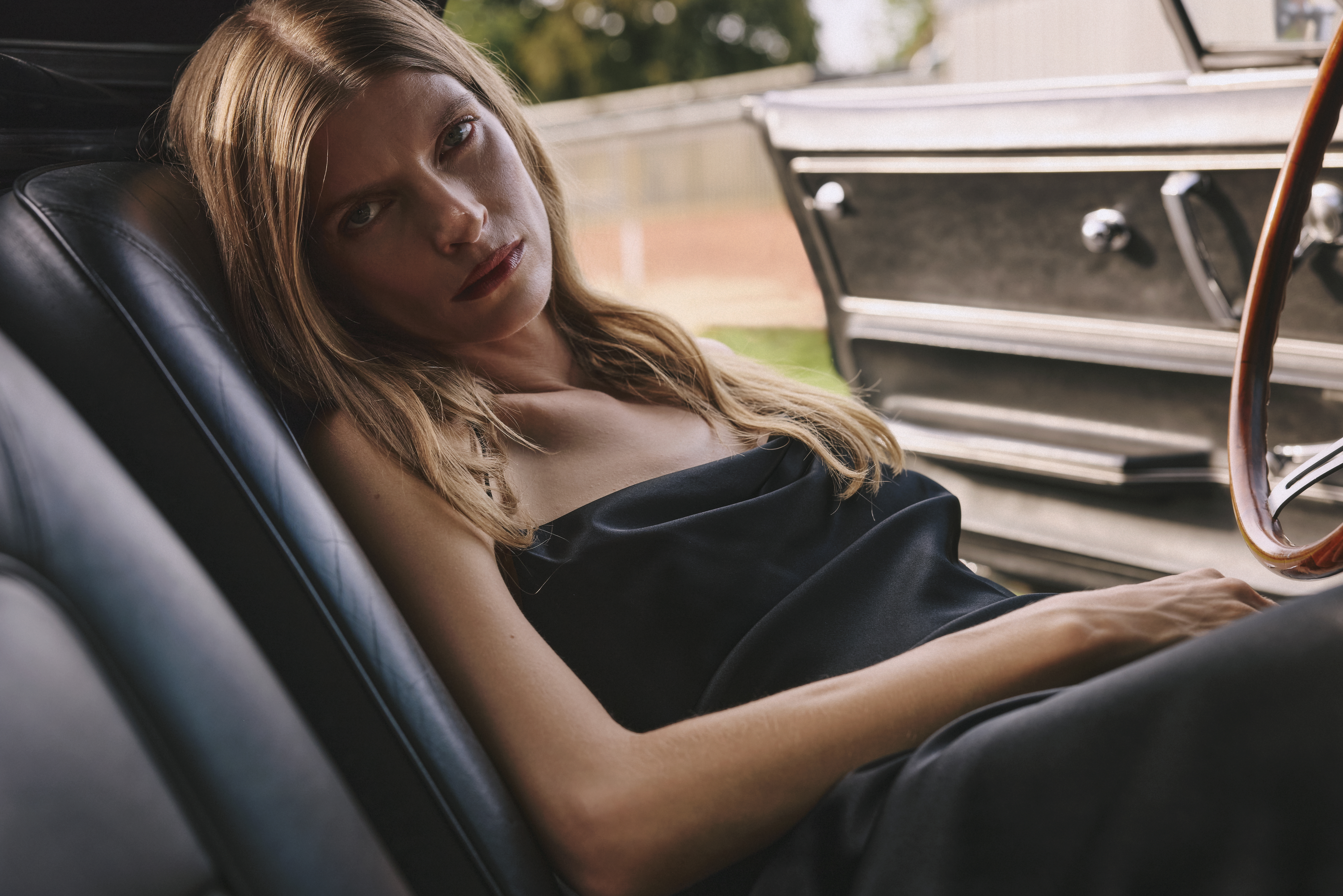 a woman is sitting in a car waering a black satin dress