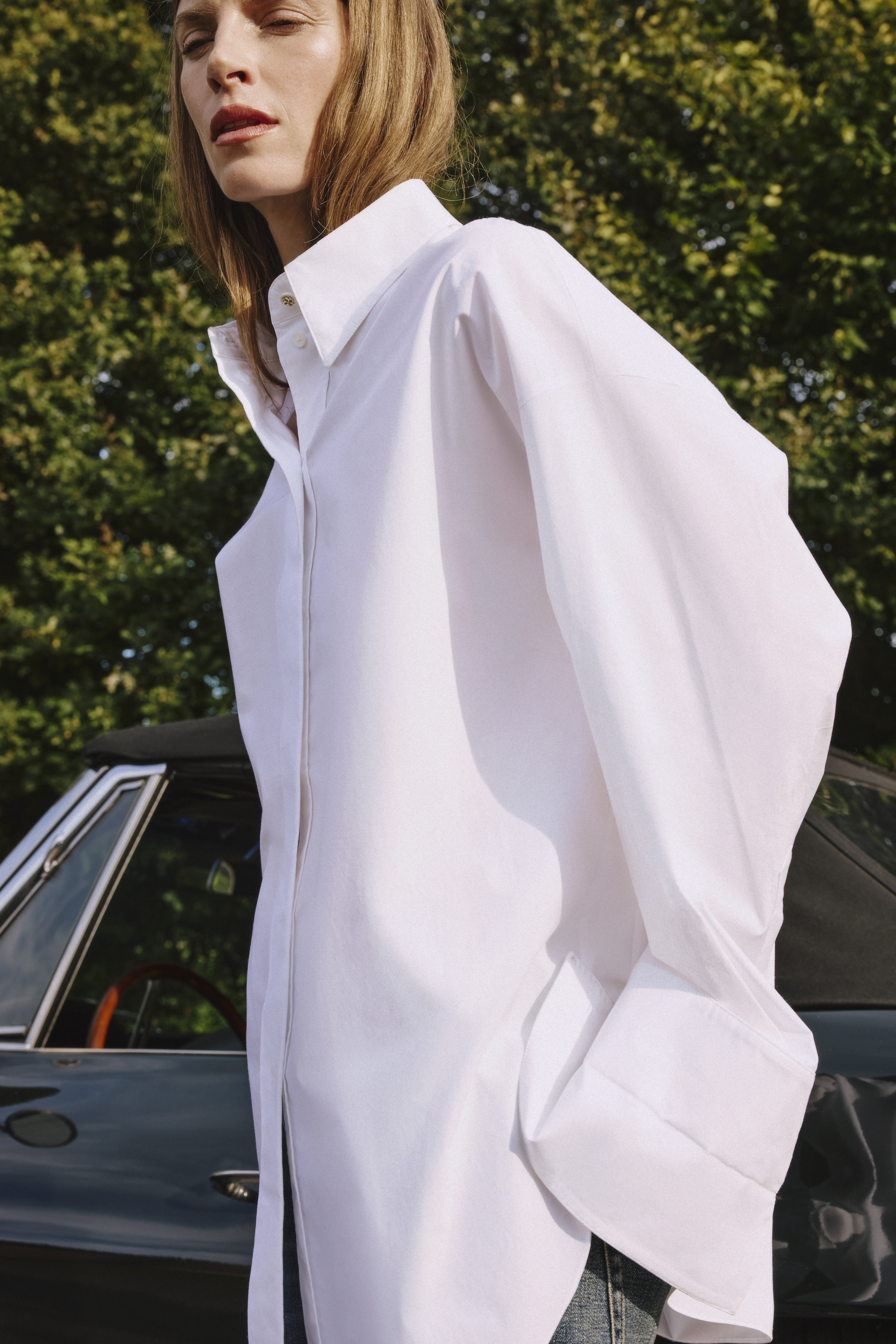 a woman is standing in front of a car wearing a white cotton blouse 