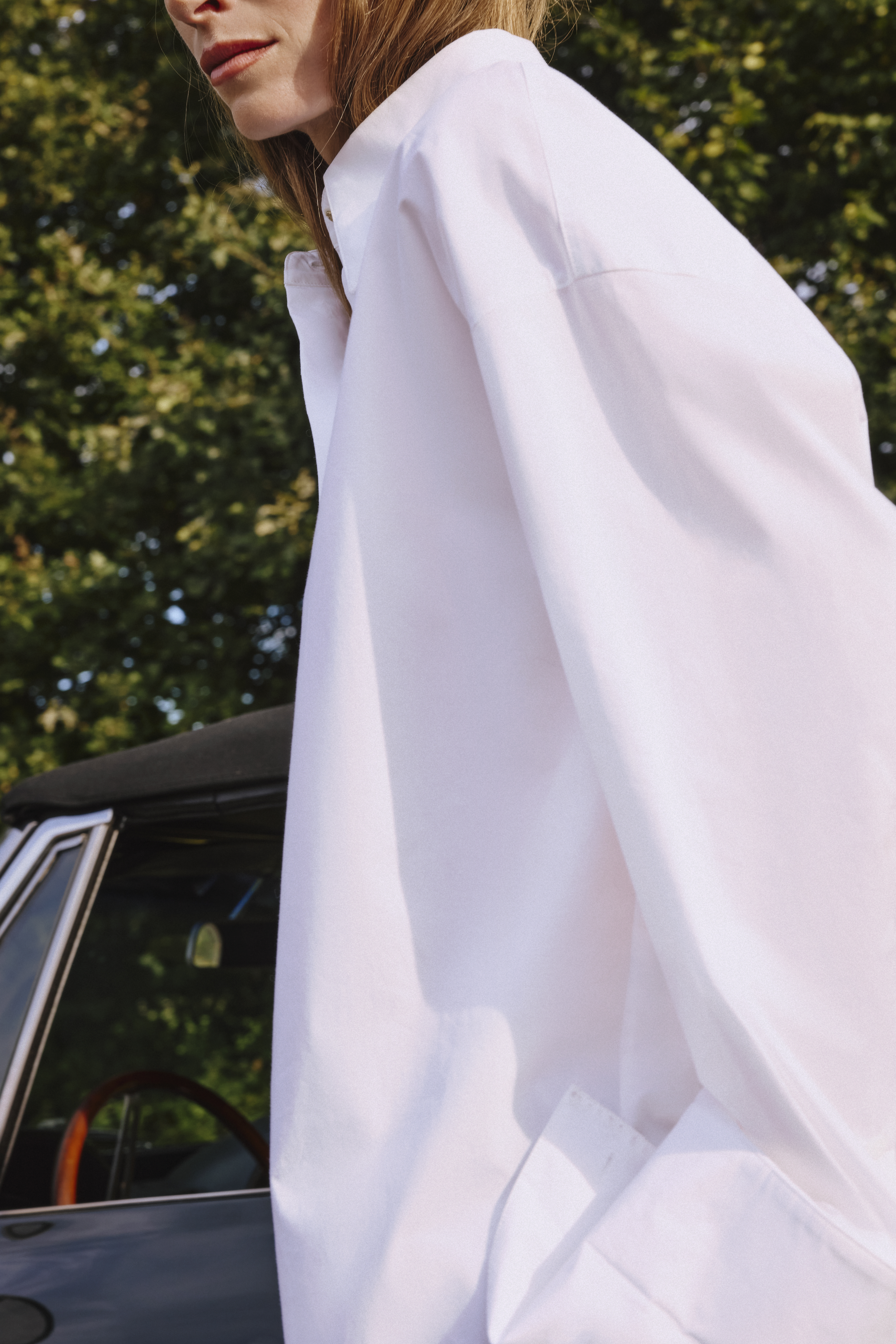 a woman is standing in front of a car wearing a white cotton blouse 