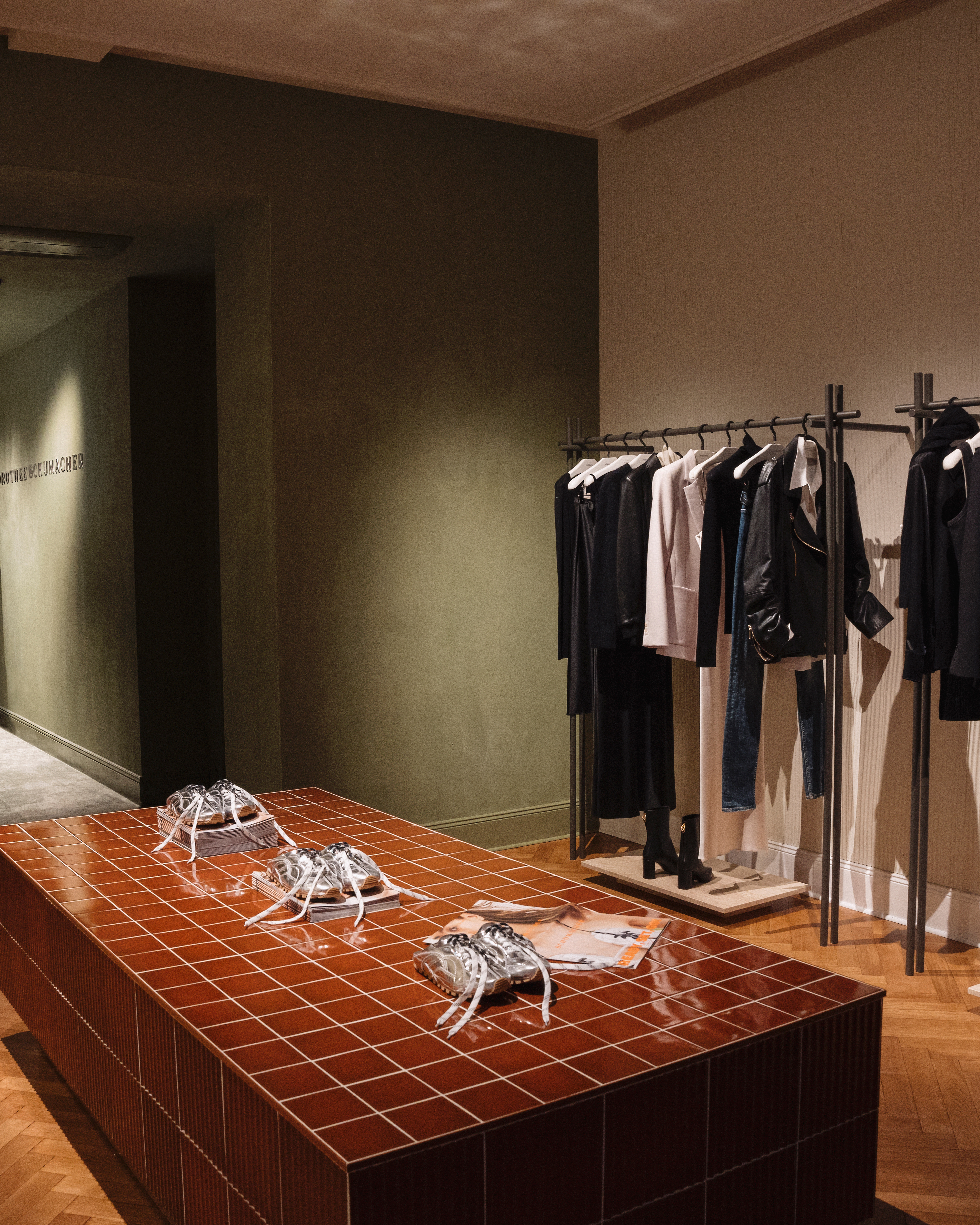 Innenansicht des Dorothee Schumacher Geschäfts mit Kleiderständern voller Damenbekleidung und einem gefliesten Präsentationstisch.