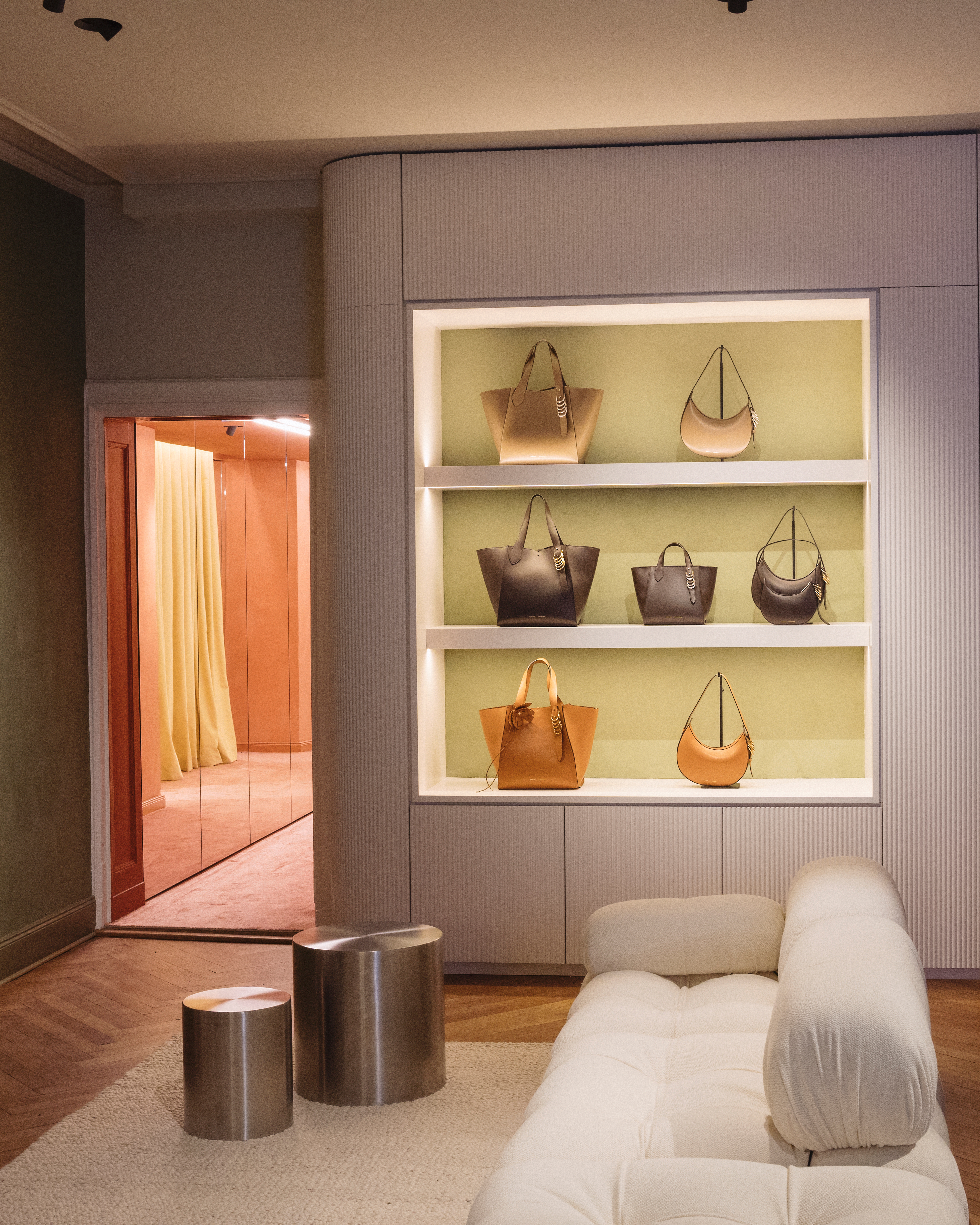 Regale mit verschiedenen Dorothee Schumacher Handtaschen und einem weißen Sofa in einem luxuriösen Ladeninterieur.