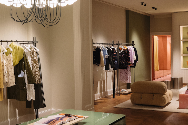 Helles und geräumiges Interieur des Dorothee Schumacher Geschäfts mit einem modernen Kronleuchter, Kleiderständern und einer gemütlichen Sitzecke.