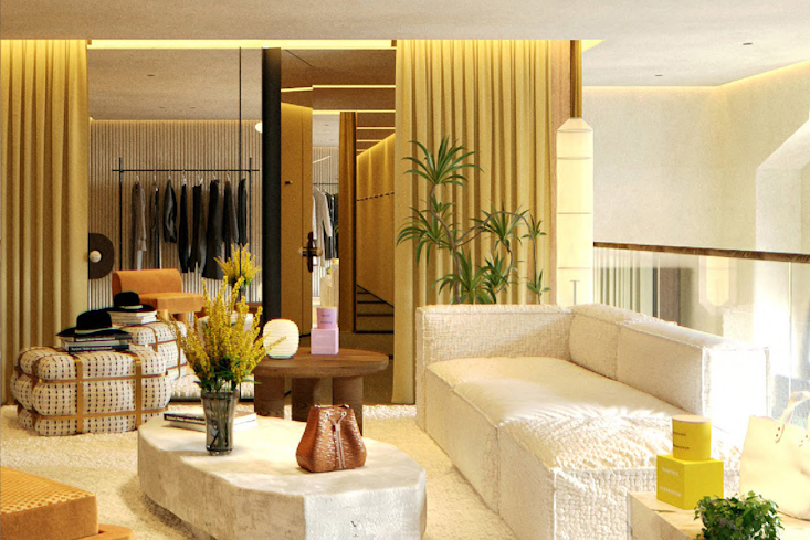 Ein stilvoller Lounge-Bereich im Dorothee Schumacher Geschäft mit einem bequemen weißen Sofa, einem Couchtisch, Pflanzen und Kleiderständern im Hintergrund, umgeben von gelben Vorhängen.