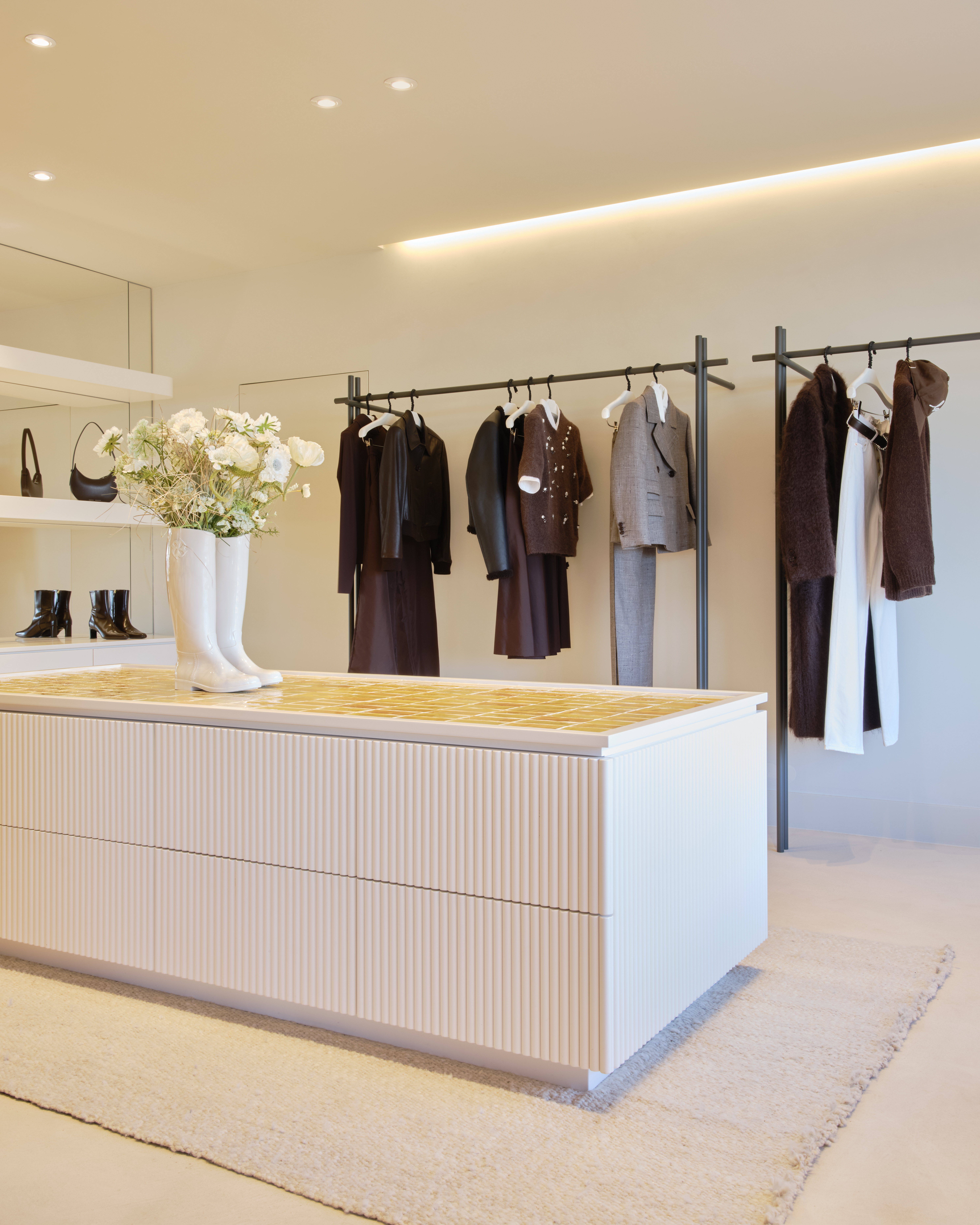 Heller Verkaufsraum im Dorothee Schumacher Geschäft mit einer weißen Auslage, Kleiderständern und einer Vase mit weißen Blumen als Dekoration.